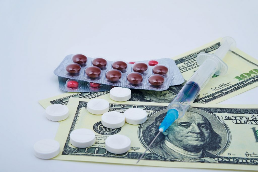 100 dollar bills with medication, medicine, pills on top of it and needle, syringe with medicine inside, expensive drug costs, prescription medicine for diabetes