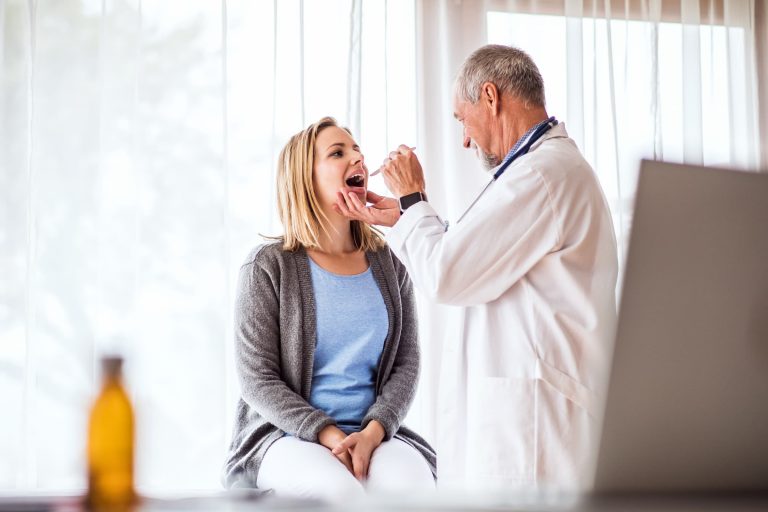 ent doctor examining a young patient in office for allergies looking at her throat as she sits on an exam table