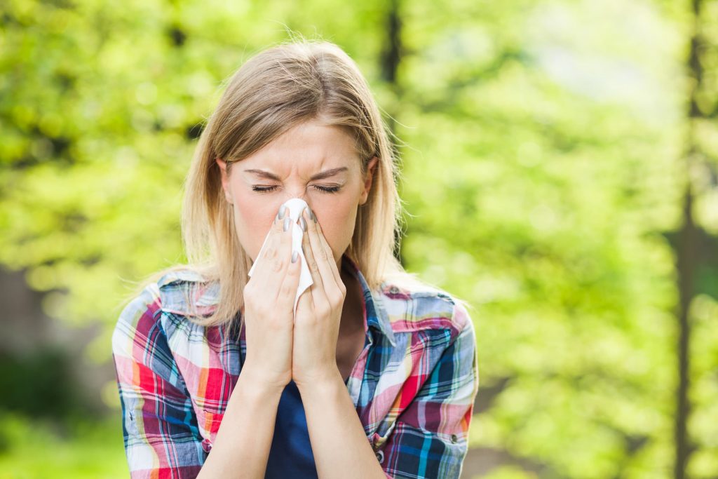 Woman with allergy symptom blow her nose, outside, spring, flu