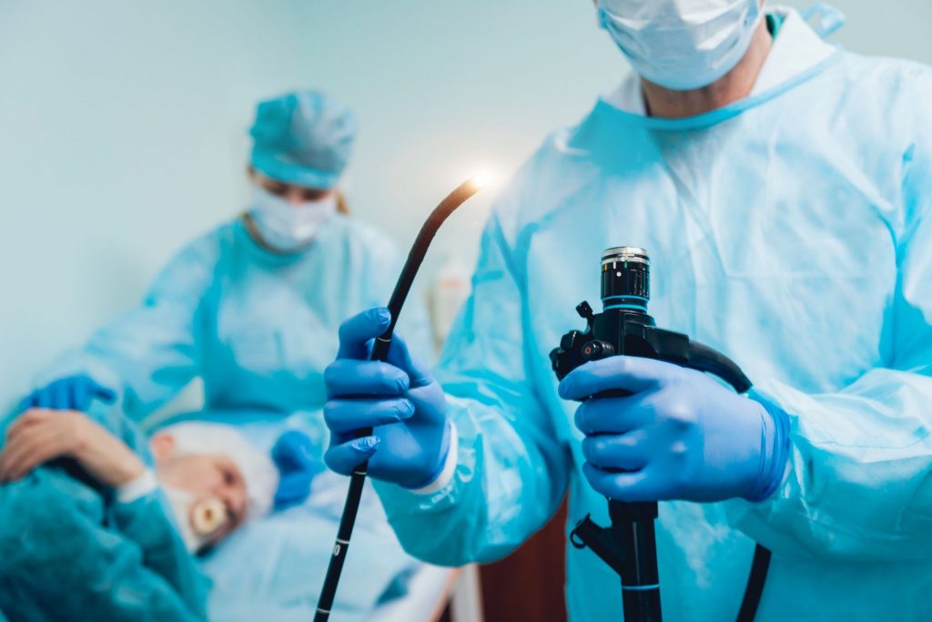doctor holding lighted scope preparing for colonoscopy with patient on table in the background ready for colonoscopy procedure routine colonoscopy