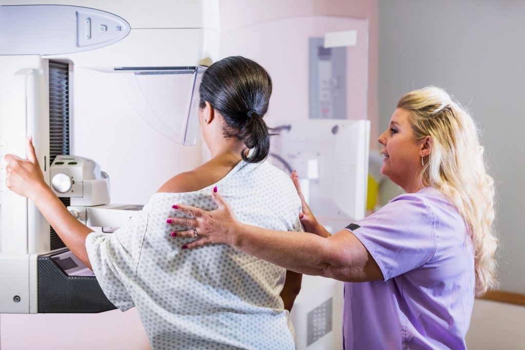 mammogram with black patient and white nurse tech and mammogram machine with backs to camera