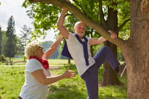 Old man climbing with senior woman on a tree in a summer park