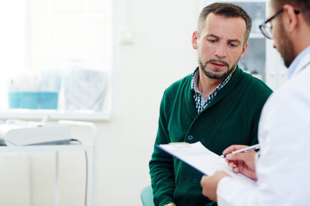 middle-aged white man in green sweater speaking with arab doctor in white coat