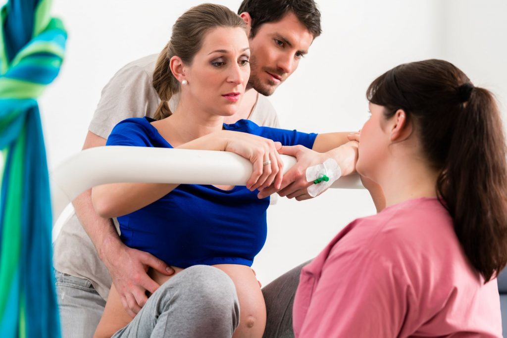 white man standing behind pregnant wife in active labor offering support as nurse walks them through process