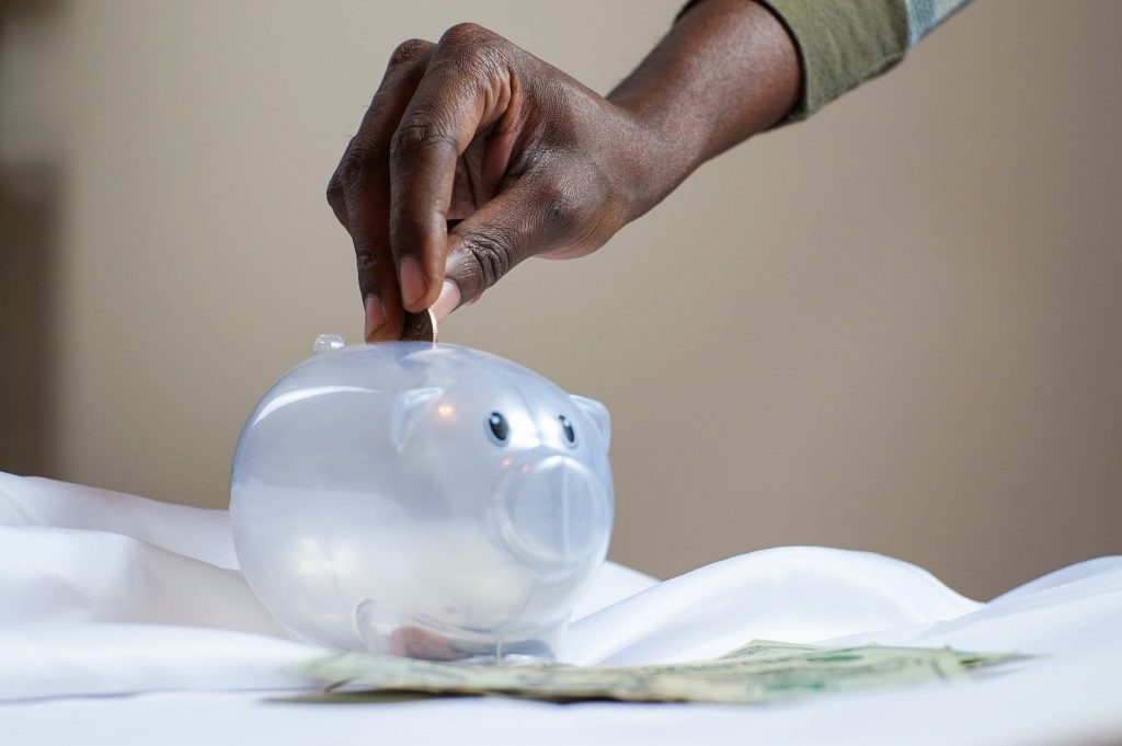 black man putting money into a clear pig-shaped piggy bank