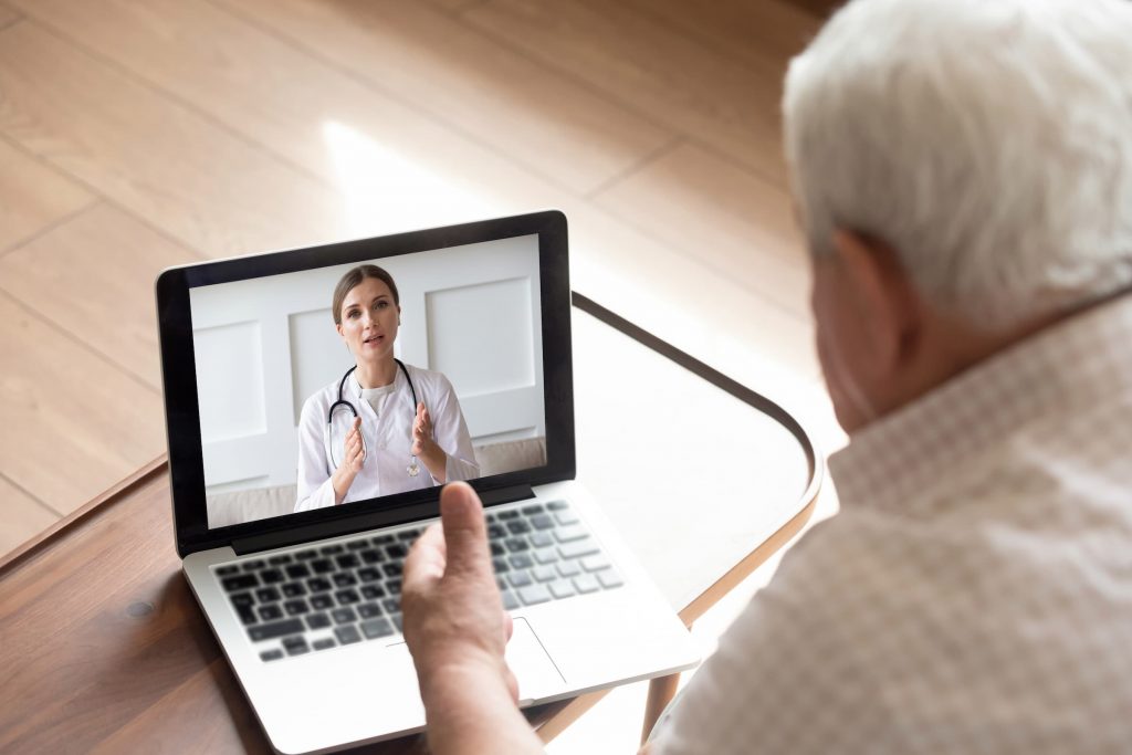 white senior man doing telemedicine visit with female brunette doctor on laptop macbook air
