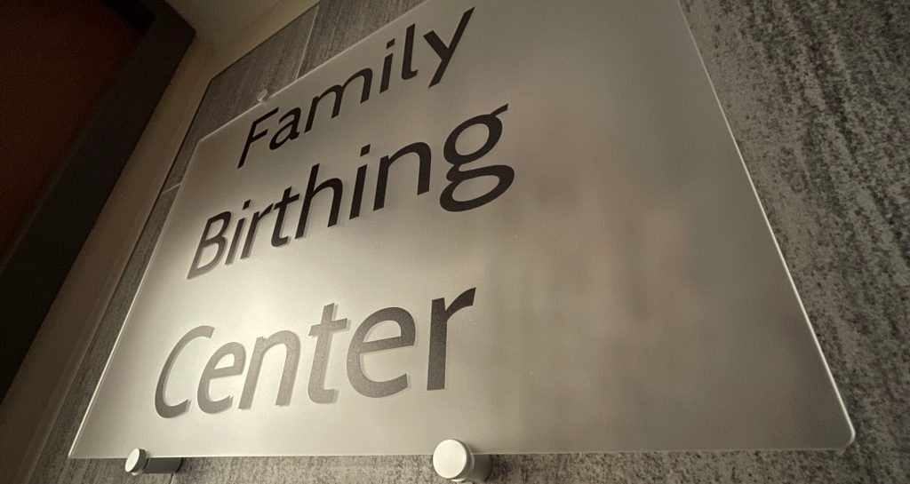 A close-up, angled shot of a frosted glass sign mounted on a wall. The sign features the words "Family Birthing Center" in a clean, dark sans-serif font.