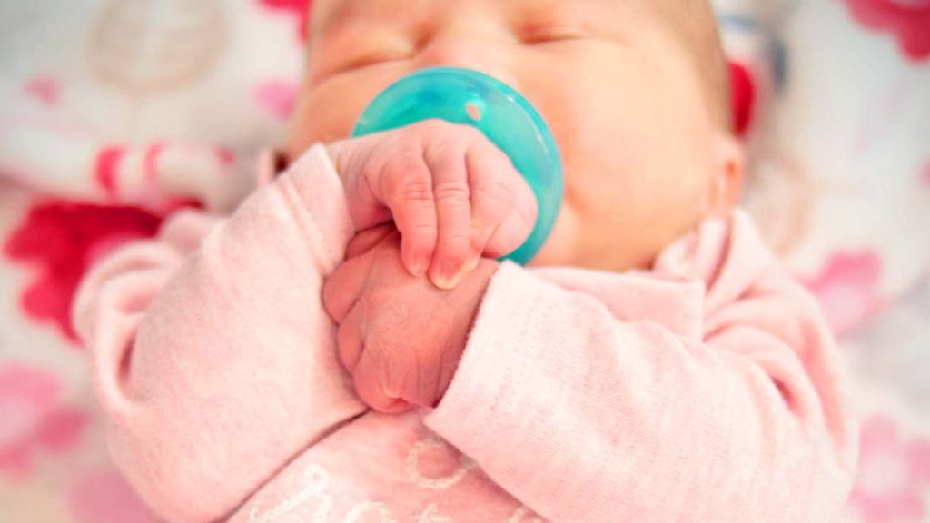 Newborn baby holds hands while sleeping on colorful blanket