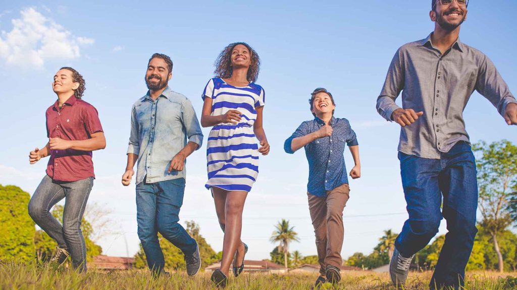 five people walk through a grassy field enjoying the outdoors with blue skies