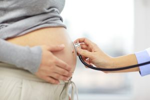 Stethoscope held to pregnant woman stomach by the gynecology doctor