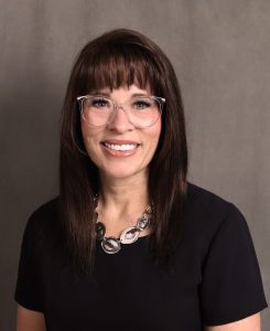Woman in glasses and a black shirt smiling at the camera