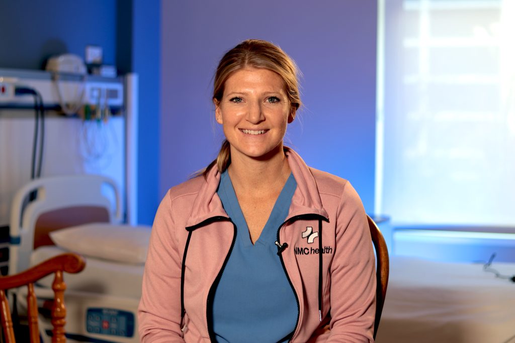 woman in nurses uniform smiling at the camera while seated in a hospital room