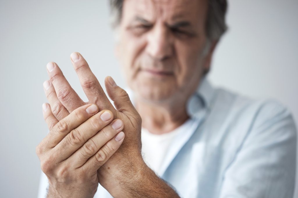 older man clutching hand in pain because of arthritis