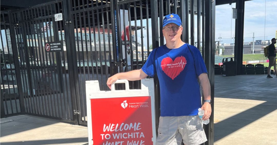 Man wearing blue shirt with red heart graphic standing next to Heart Walk sign