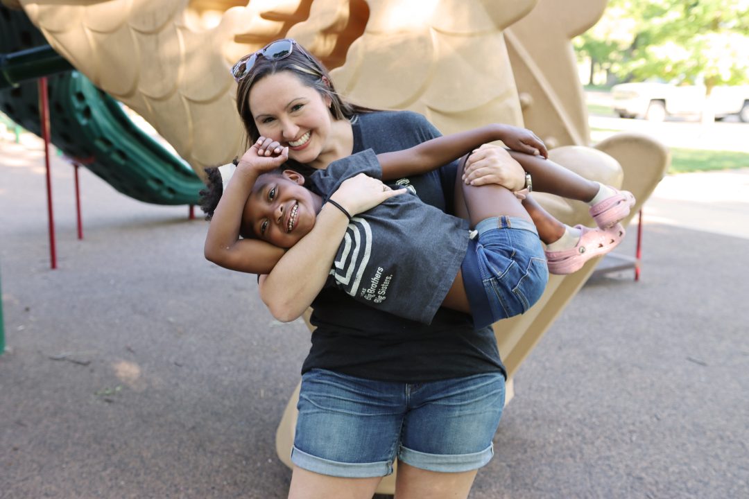 smiling young woman holding smiling, young african american girl at playground