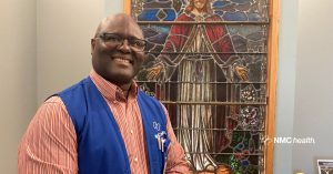 smiling african-american man wearing blue vest standing in front of chapel stained glass