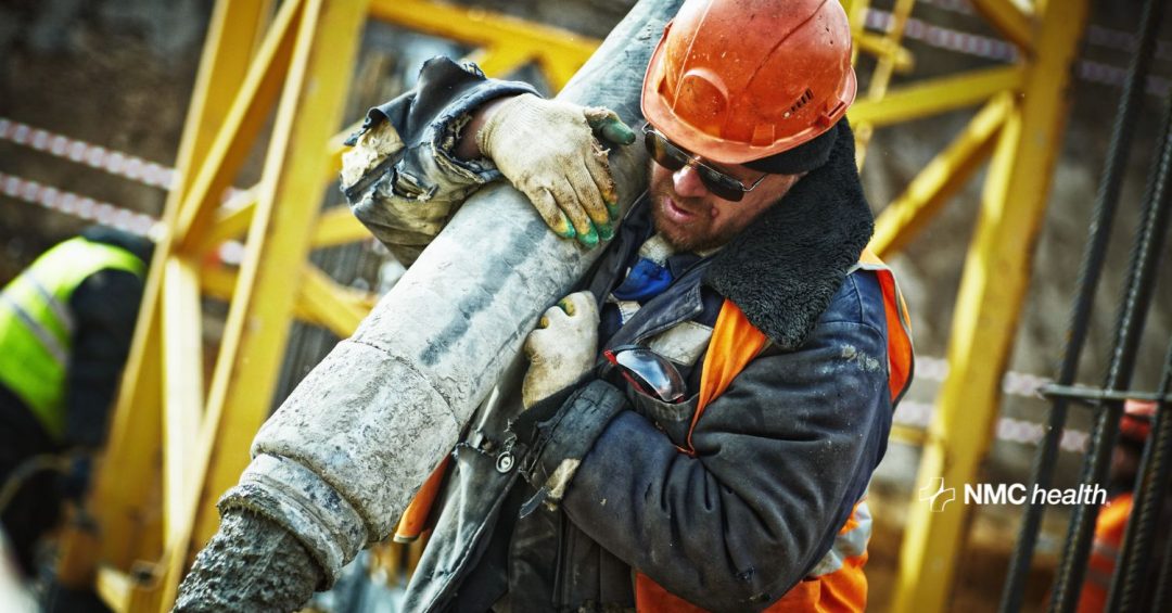 construction worker wearing orange helmet and vest lifting and carrying heavy object