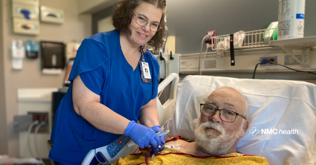 male dialysis patient in hospital bed with smiling nurse in blue scrubs