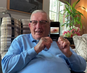 man sitting in chair holding up cell phone next to face showing picture of arm wound