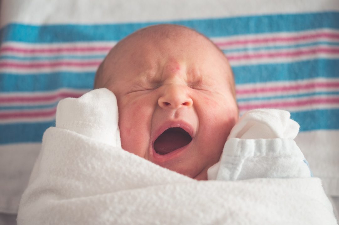 newborn baby swaddled and laying on hospital receiving blanket yawning and scrunching face
