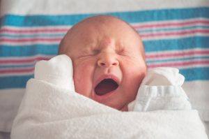 newborn baby swaddled and laying on hospital receiving blanket yawning and scrunching face
