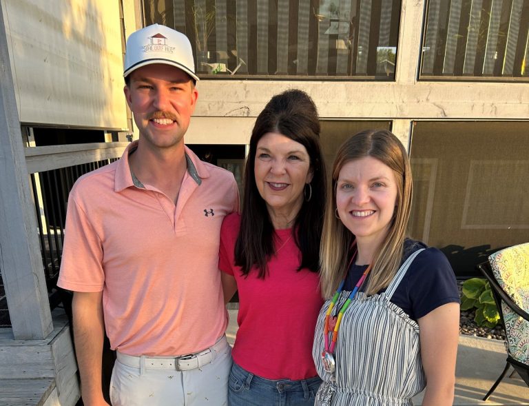 man wearing polo and cap stands next to two women