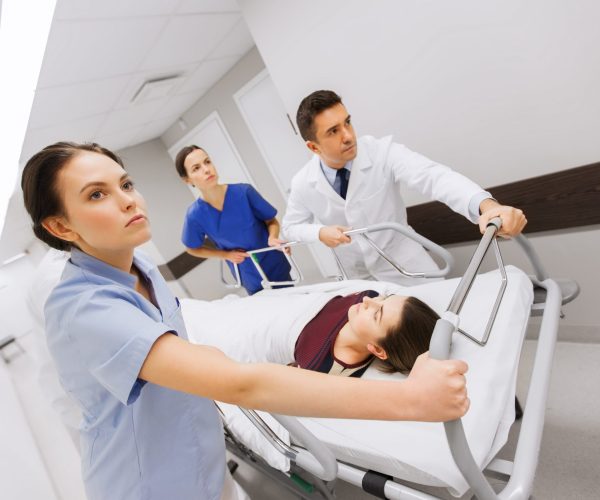 profession, people, health care, reanimation and medicine concept - group of medics or doctors carrying woman patient on hospital gurney to emergency
