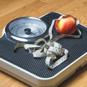 Weight Loss weight with measuring tape and apple sitting on top of it on the floor weight management manage your weight weight loss